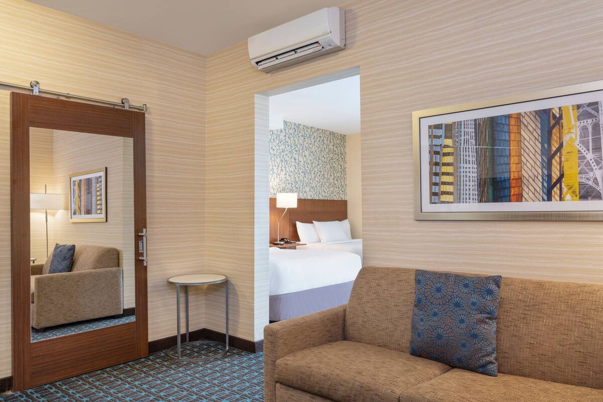 A hotel room with a bed, a sofa, a small table, a mirror, and a framed picture on the wall.