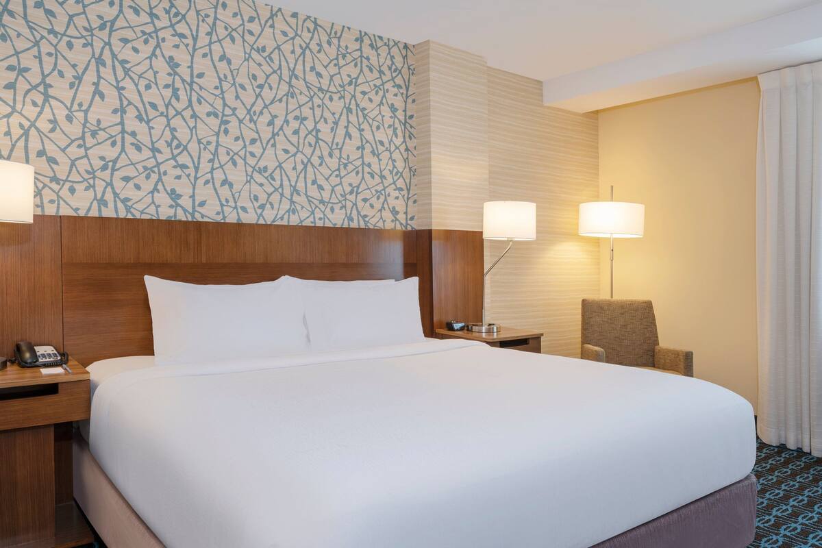 A hotel room with a large bed, two bedside tables, a chair, and a patterned wall.