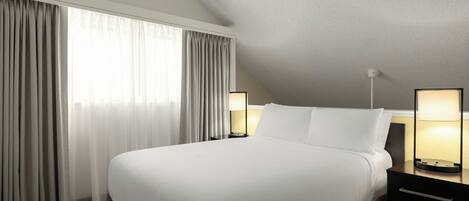 A hotel room with a large bed, two bedside tables with lamps, a window with curtains, and a textured ceiling.