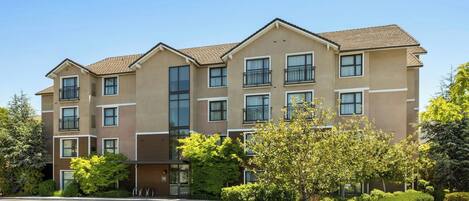 A multi-story residential building with a parking lot and landscaped greenery.
