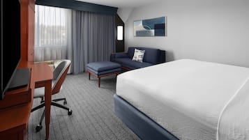 A hotel room with a bed, a desk with a chair, a sofa, and a window with curtains.