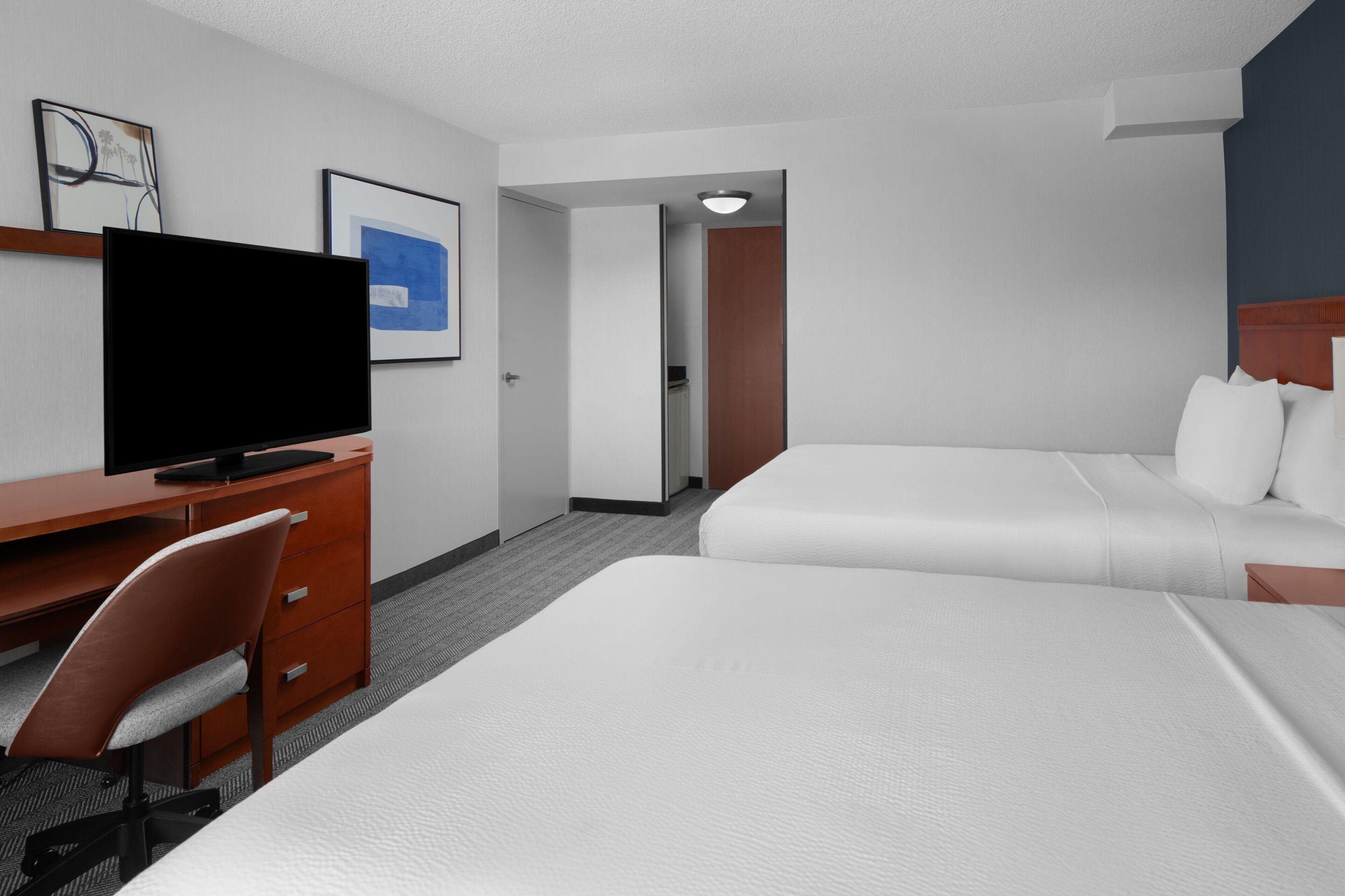 A hotel room with a bed, a desk with a chair, a television, and a door leading to another room.