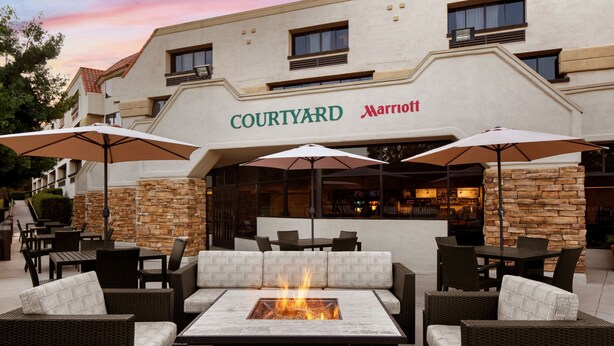 Zona de estar exterior en un Courtyard Marriott con mobiliario de mimbre, una chimenea y detalles de piedra.