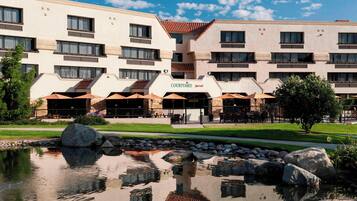 Un hotel Courtyard Marriott con piscina reflectante, mobiliario exterior y césped bien cuidado.