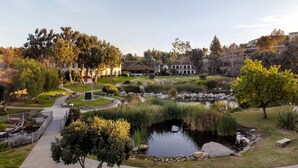 Un jardín ajardinado con un estanque, senderos y un edificio al fondo.