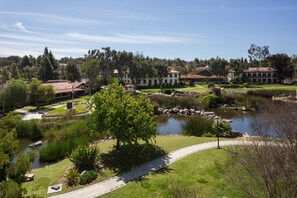 Stroll through the tranquil garden, featuring a serene pond and walking path, surrounded by lush greenery and the main hotel building.