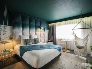 Une chambre d’hôtel moderne avec un grand lit, un fauteuil suspendu, une petite table et une vue sur l’extérieur.