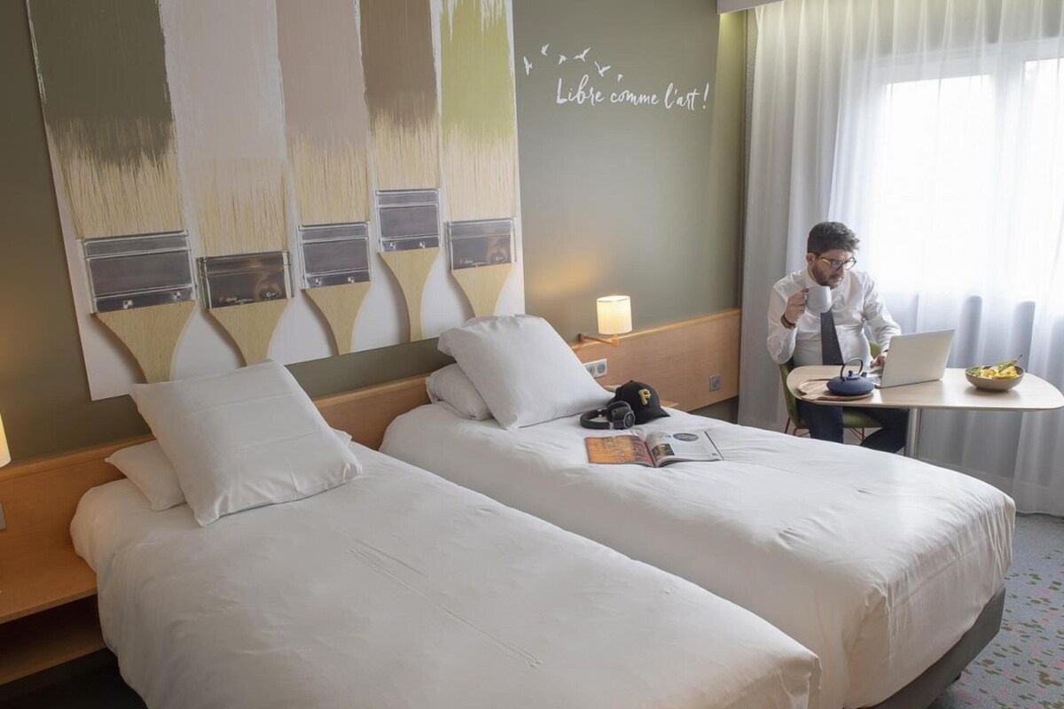 A hotel room with two beds, a desk, and a laptop.