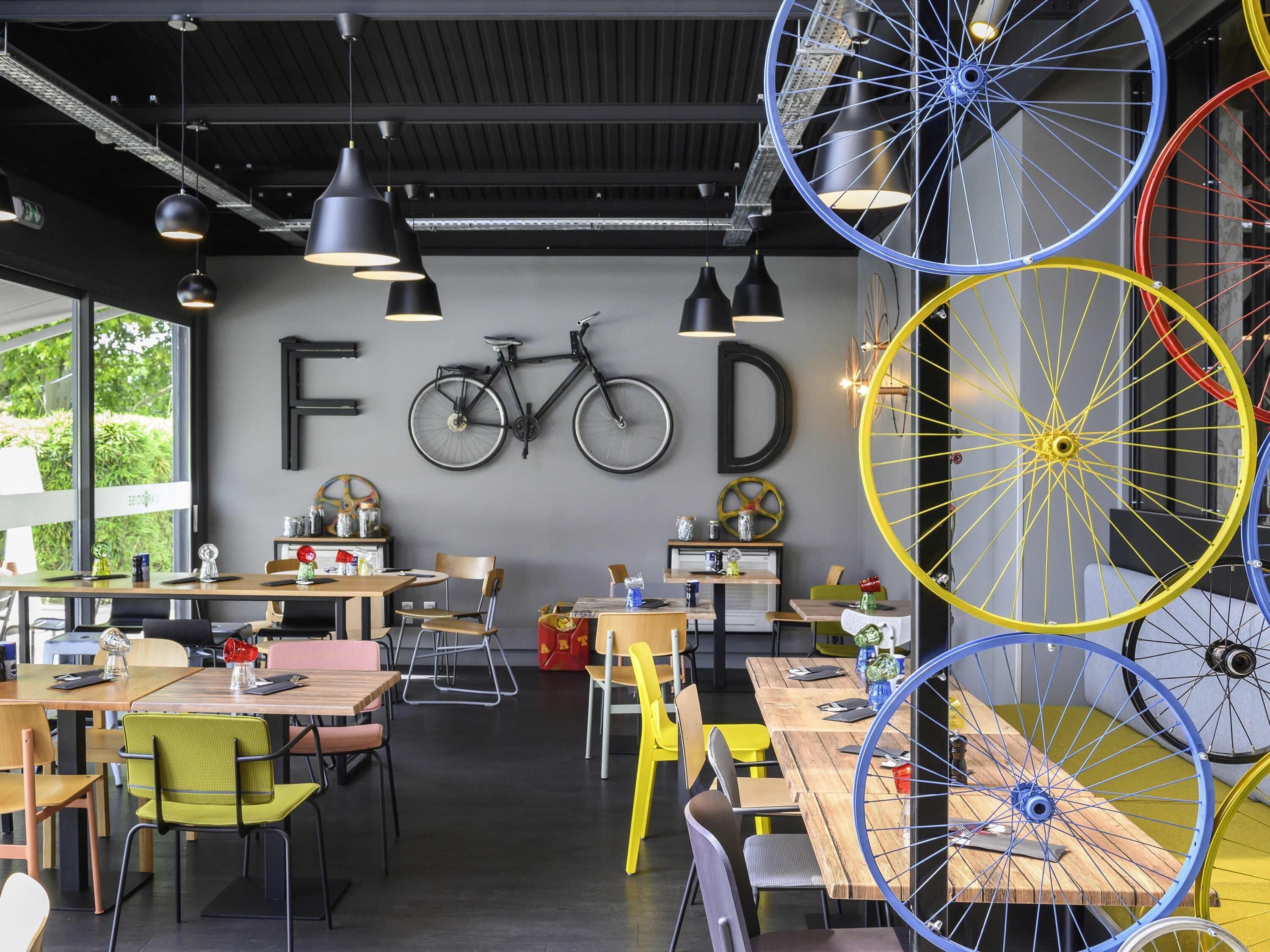 A modern cafe with wooden tables and chairs, a bicycle mounted on the wall, and large bicycle wheels as decor.