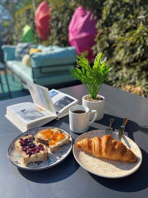 A table with a croissant, a plate with jam-topped toast, a coffee mug, and an open book.
