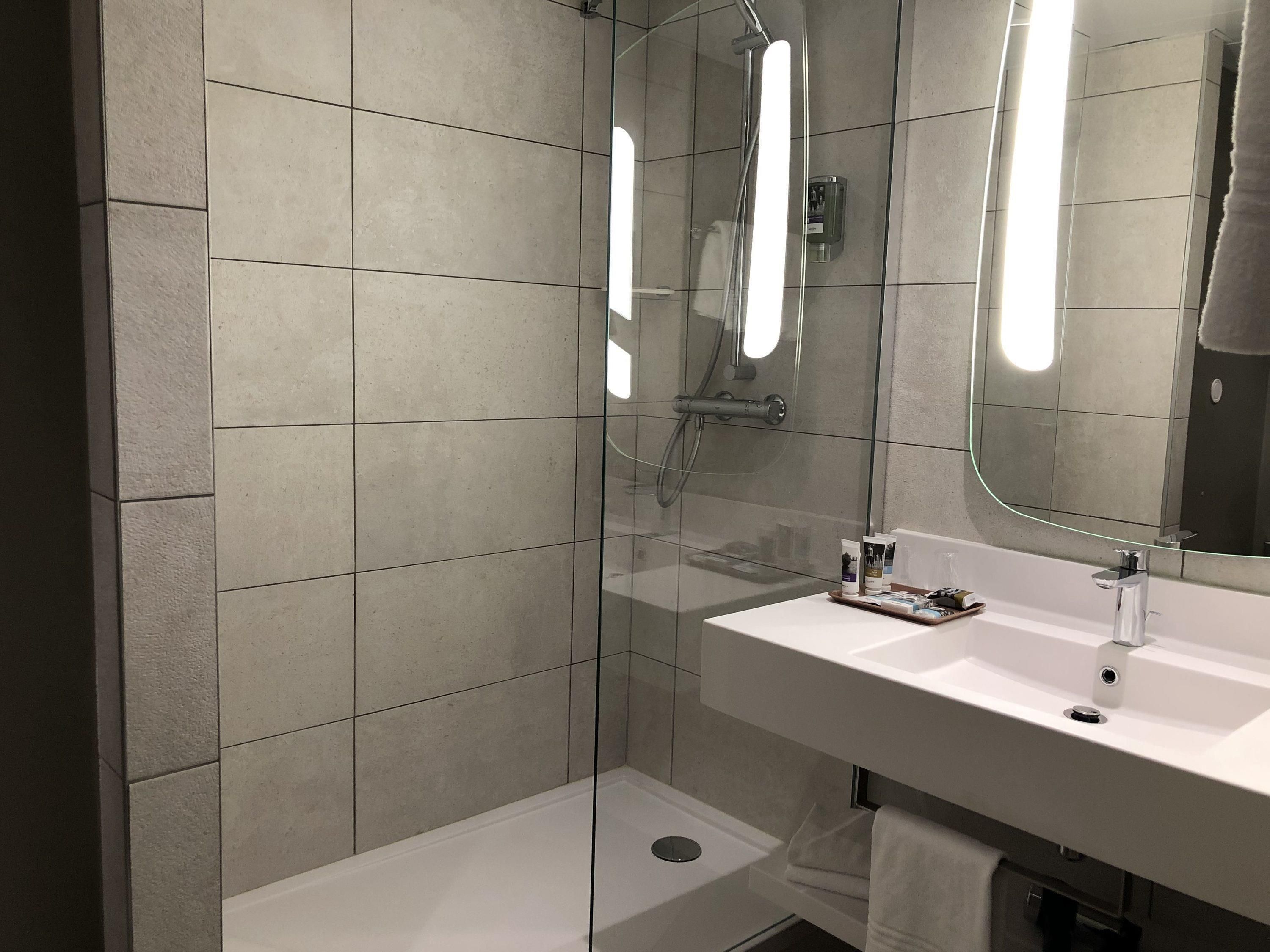 Ein modernes Badezimmer mit einer gläsernen Duschkabine, einem weißen Waschbecken und einem großen Spiegel.