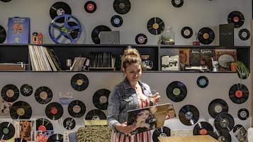 A room with a wall covered in vinyl records, a table, and a person holding a magazine.