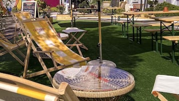 An outdoor seating area with wicker chairs and tables, a round table with a glass top, and a sign for 'Mercure OTEL' in the background.
