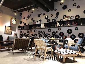 A room with a wall covered in vinyl records, wooden furniture, and a patterned rug. - Mercure Reims Parc des Expositions (Reims)