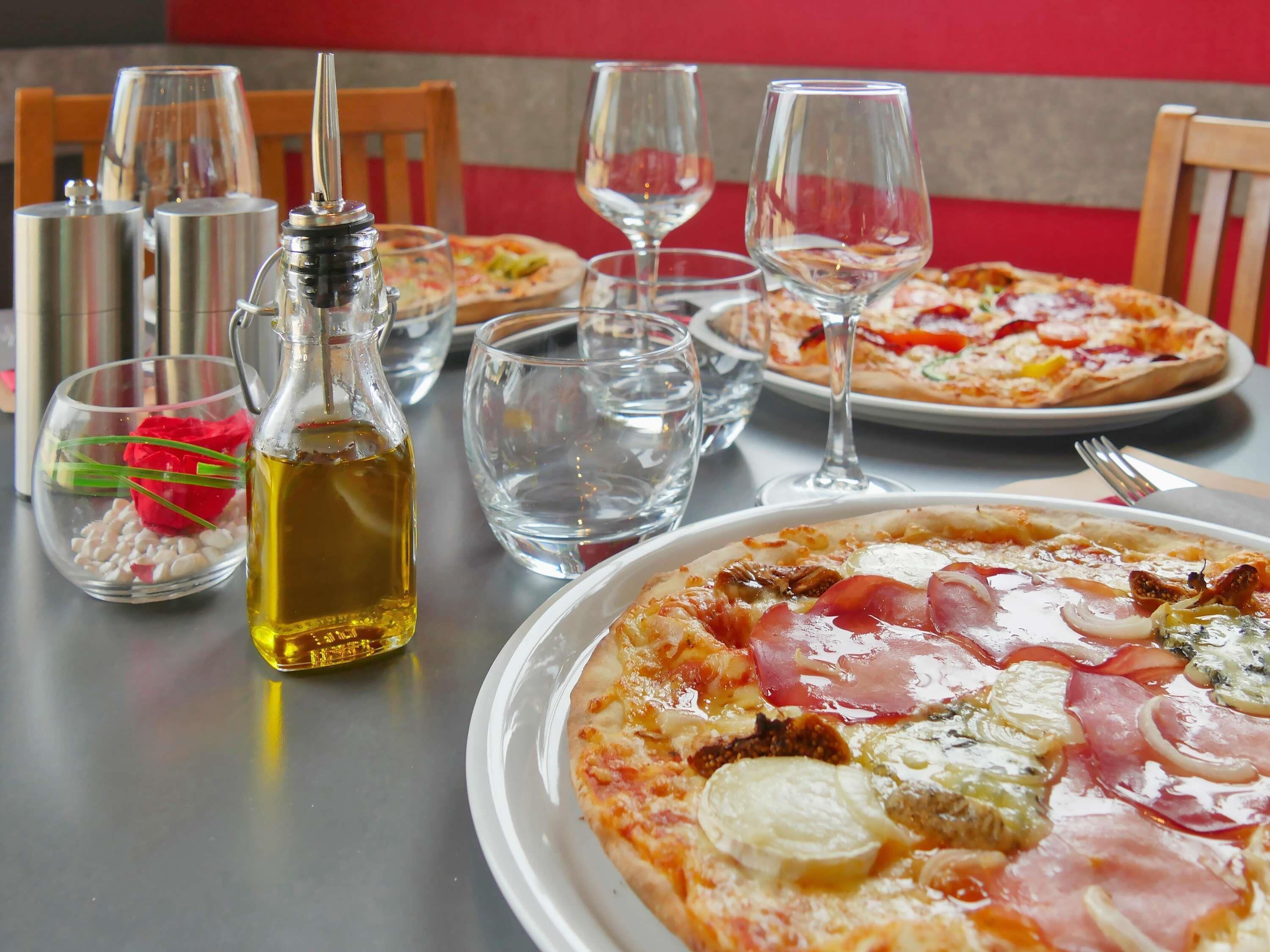 A dining table with a pizza, a bottle of olive oil, and empty wine glasses.