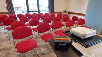 A conference room with rows of red chairs, a projector, and an ibis meeting box on a table.