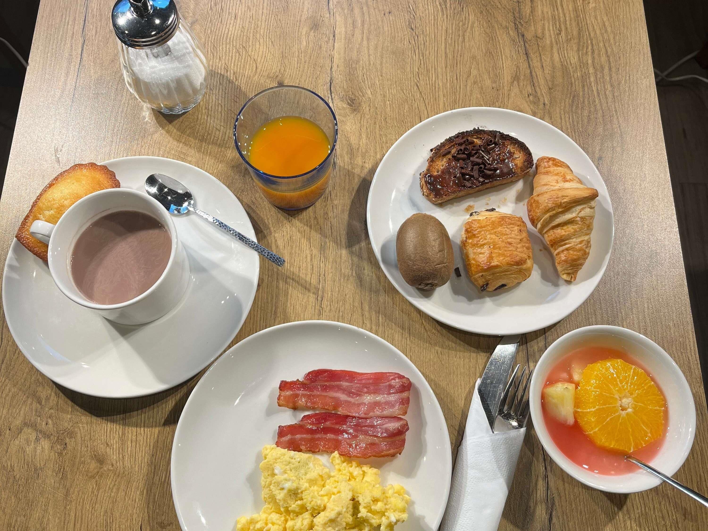 Un petit-déjeuner composé de pain grillé, d’œufs, de bacon, de croissants et d’un jus de fruits.