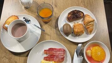 Desayuno con tostadas, huevos, tocino, cruasanes y un jugo de fruta.