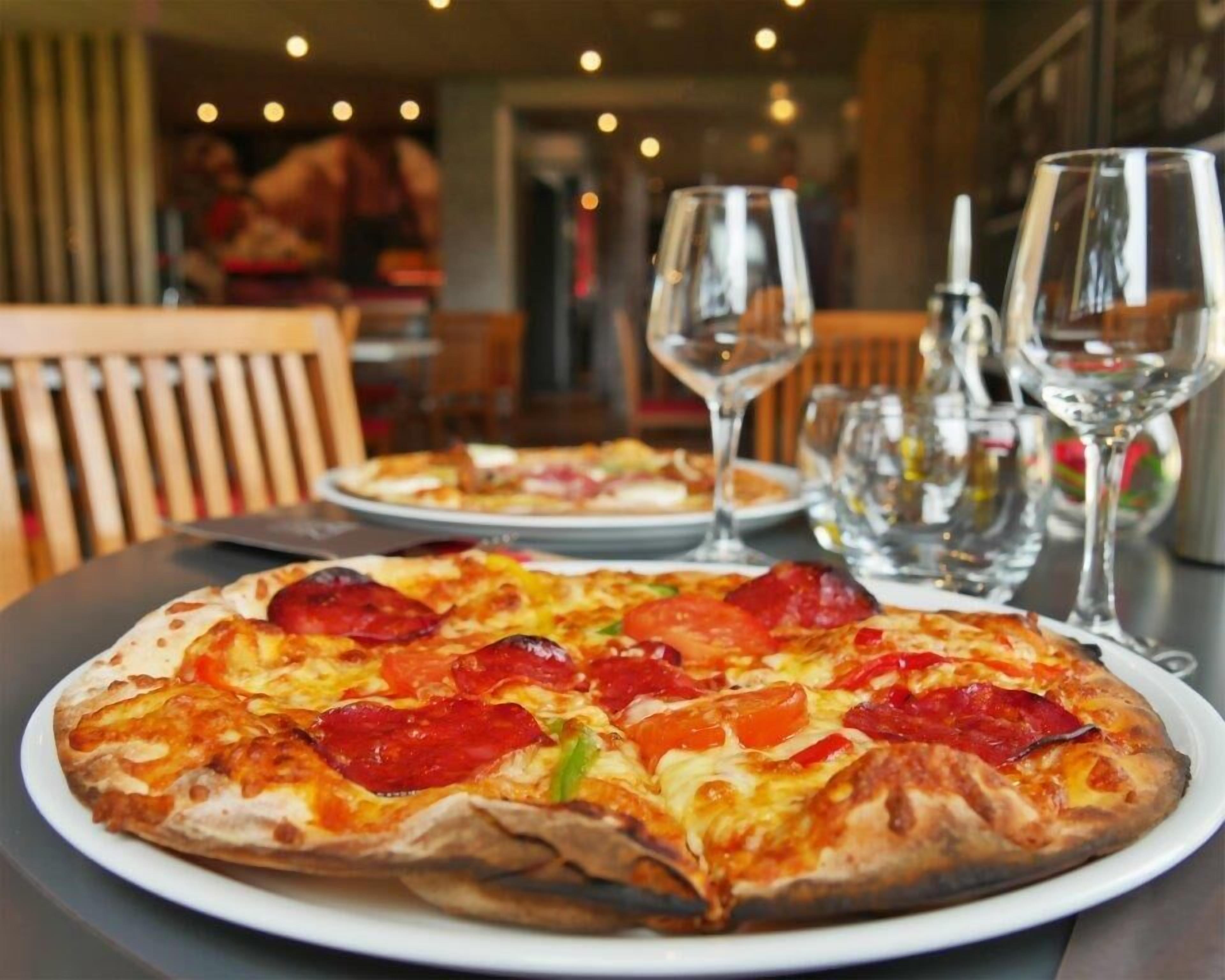 Una pizza con pepperoni y pimientos sobre un plato blanco, acompañada de dos copas de vino y un vaso de agua sobre una mesa.
