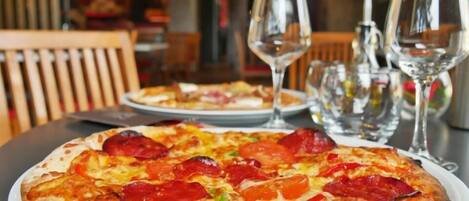 Una pizza con pepperoni y pimientos sobre un plato blanco, acompañada de dos copas de vino y un vaso de agua sobre una mesa.