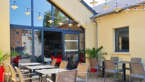 Un patio exterior con mesas y sillas, luces colgantes y plantas en macetas.