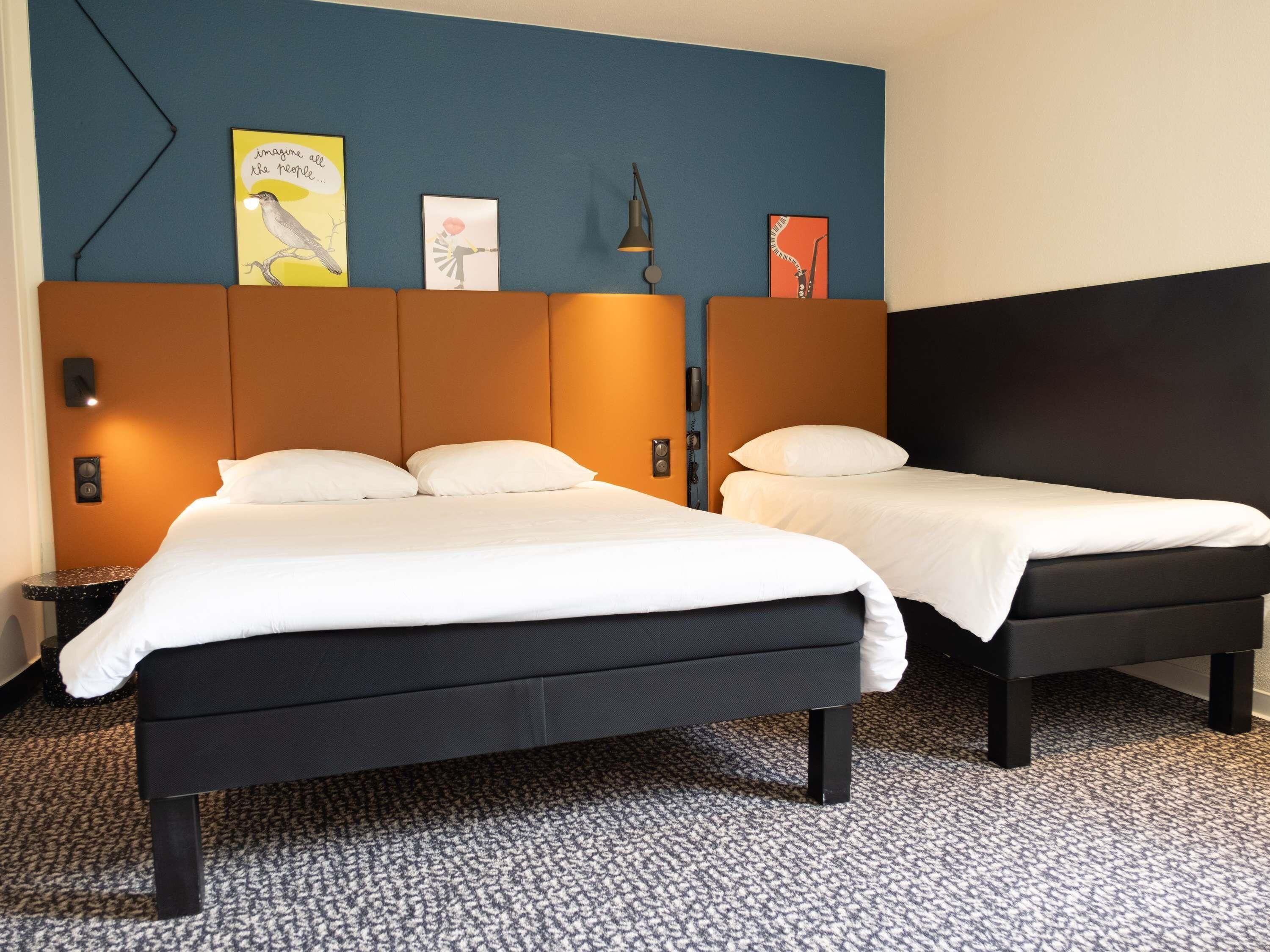 Habitación de hotel con dos camas, una pared de acento azul y obras de arte.