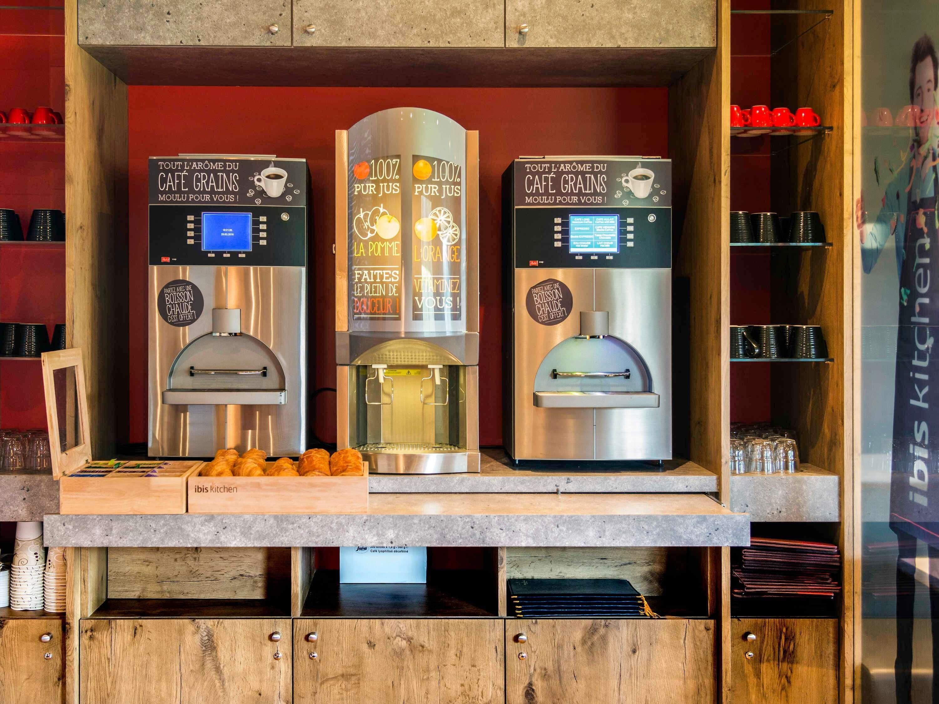Three coffee machines with digital displays, a wooden counter, and a glass display case with red cups.