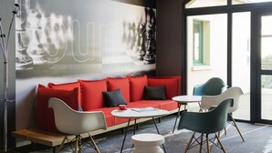 Un moderno vestíbulo de hotel con un sofá rojo, sillas blancas y turquesa, una mesa de centro y una gran obra de arte abstracto en la pared.