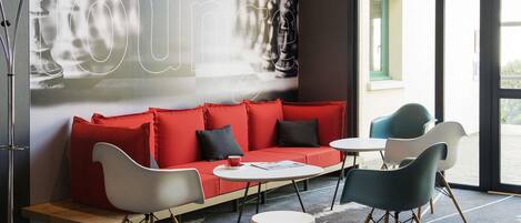 A modern hotel lobby with a red sofa, white and teal chairs, a coffee table, and a large abstract wall art piece.