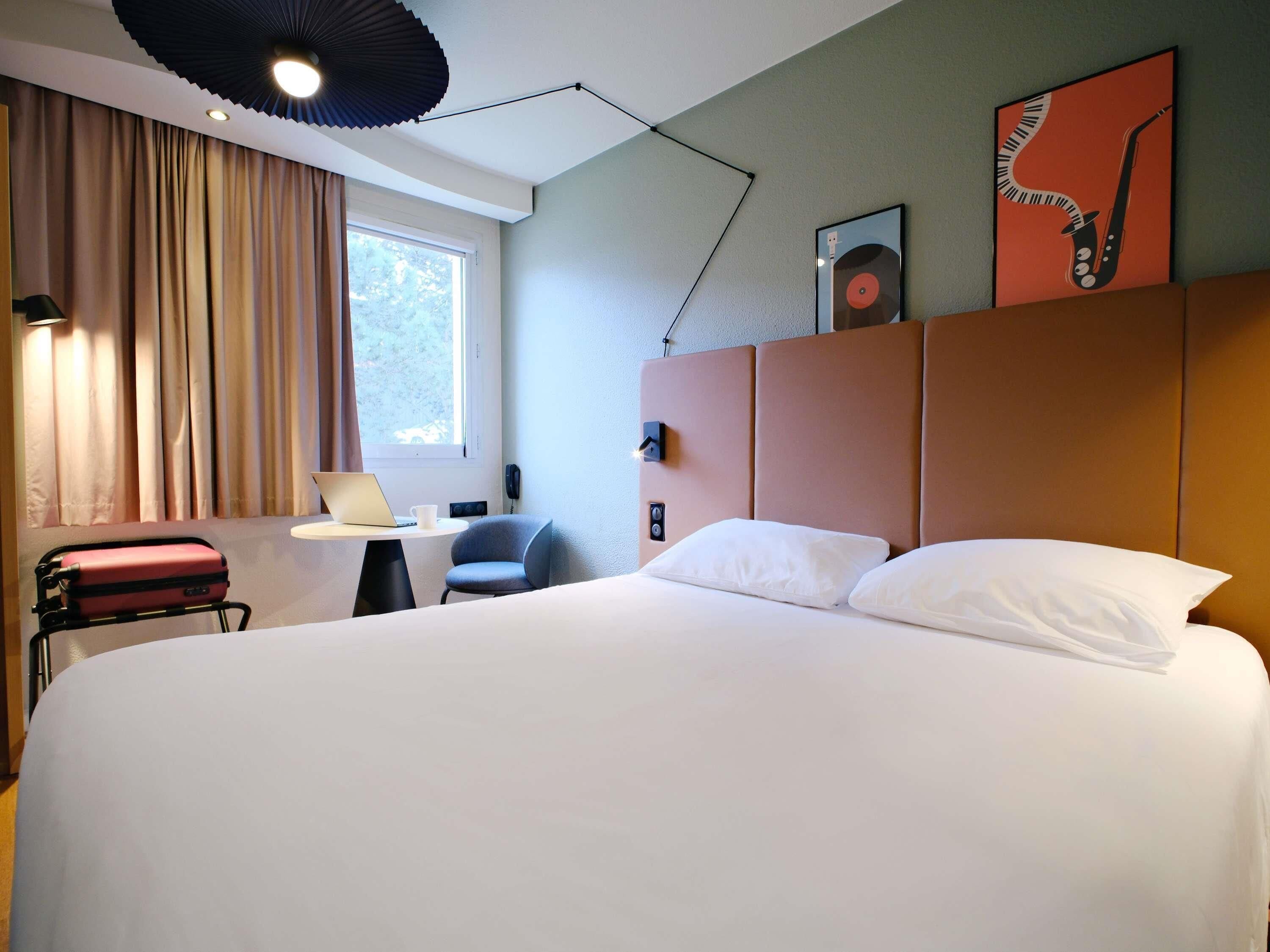 Habitación de hotel con una cama grande, un escritorio con una computadora portátil, una silla, un teléfono y una ventana con cortinas.
