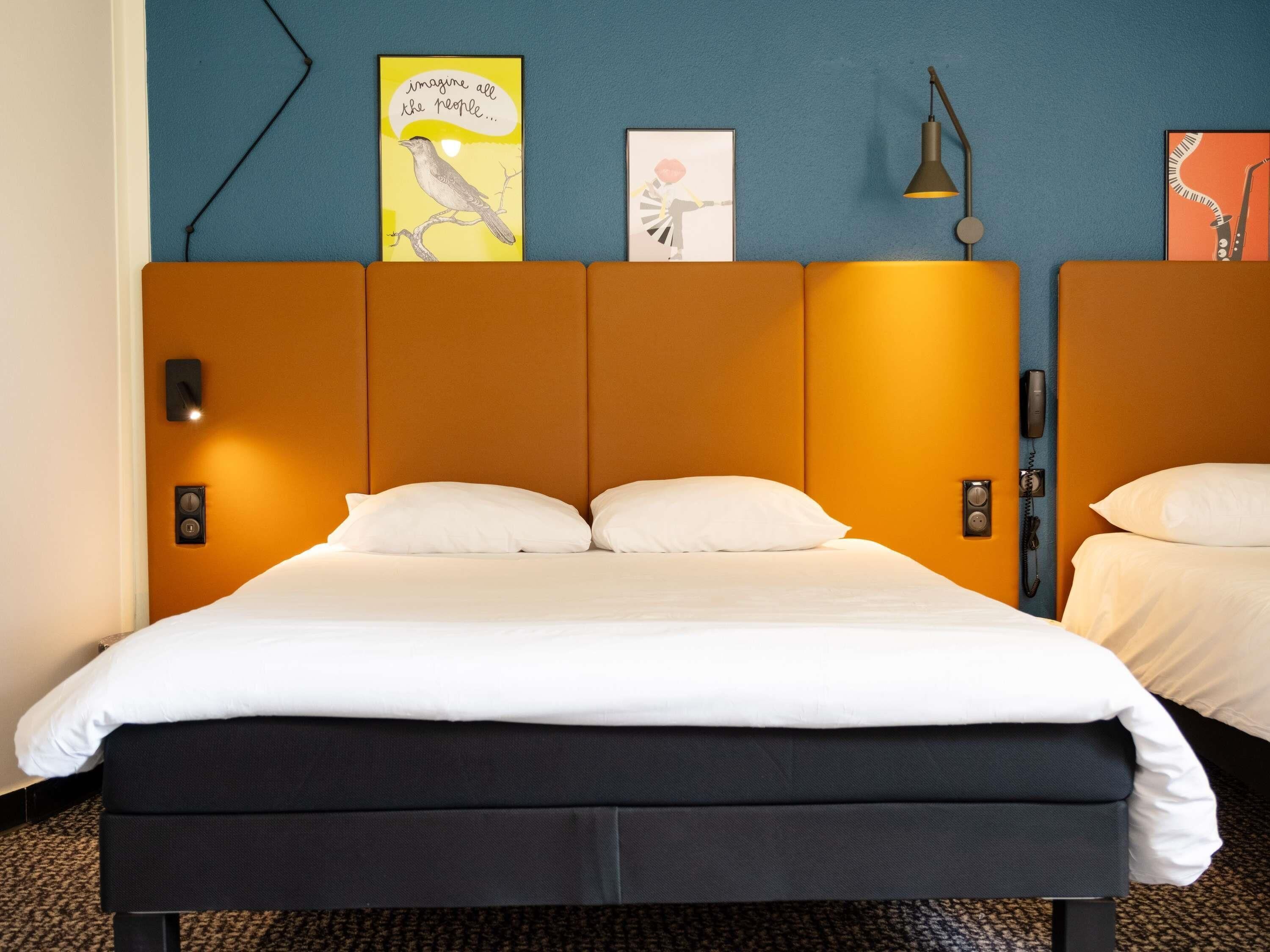 A hotel room with a bed, two bedside tables, a wall-mounted telephone, and artwork on the wall.