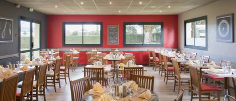 Un restaurante con varias mesas y sillas, ventanas amplias que dan a zonas verdes y una pared de acento roja.