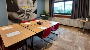 Un salón de conferencias con un mural grande en la pared, una ventana con cortinas y una pequeña mesa con vasos y una botella.