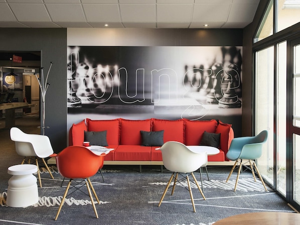 A modern lounge area with a red sofa, white and blue chairs, and a large abstract wall art piece.