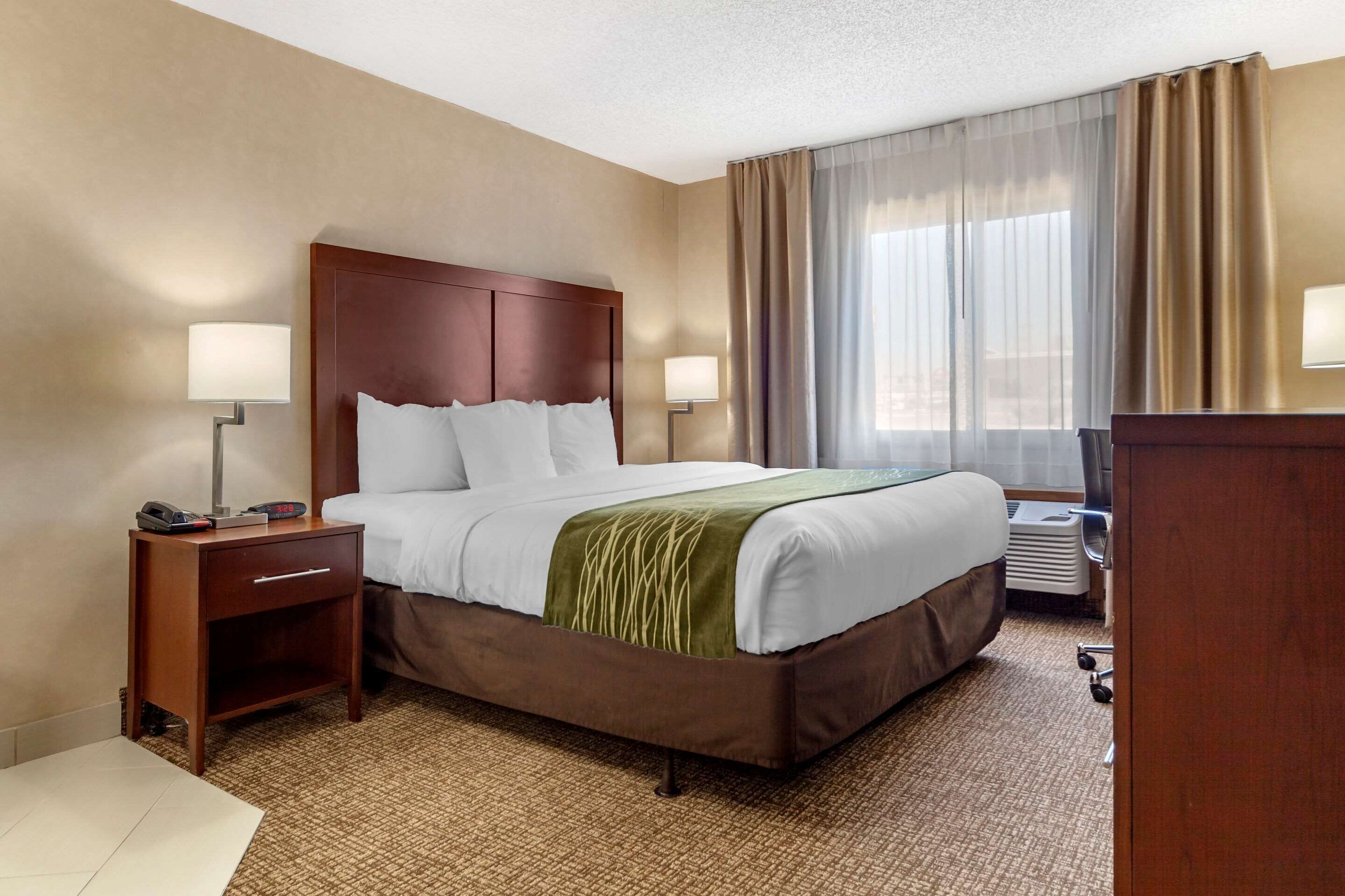 Une chambre d’hôtel avec un grand lit, deux tables de chevet avec des lampes, un bureau et une fenêtre avec des rideaux.