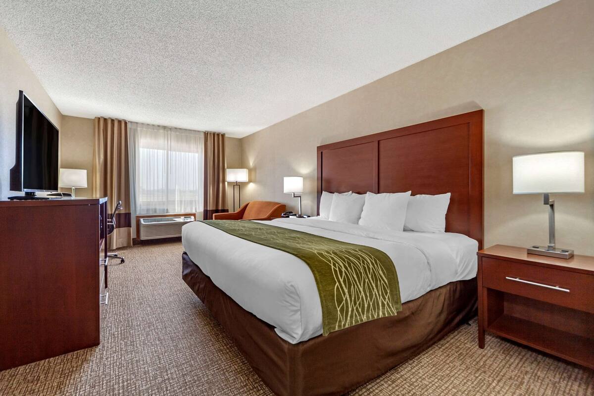 A hotel room with a large bed, a desk, a TV, and a lamp.