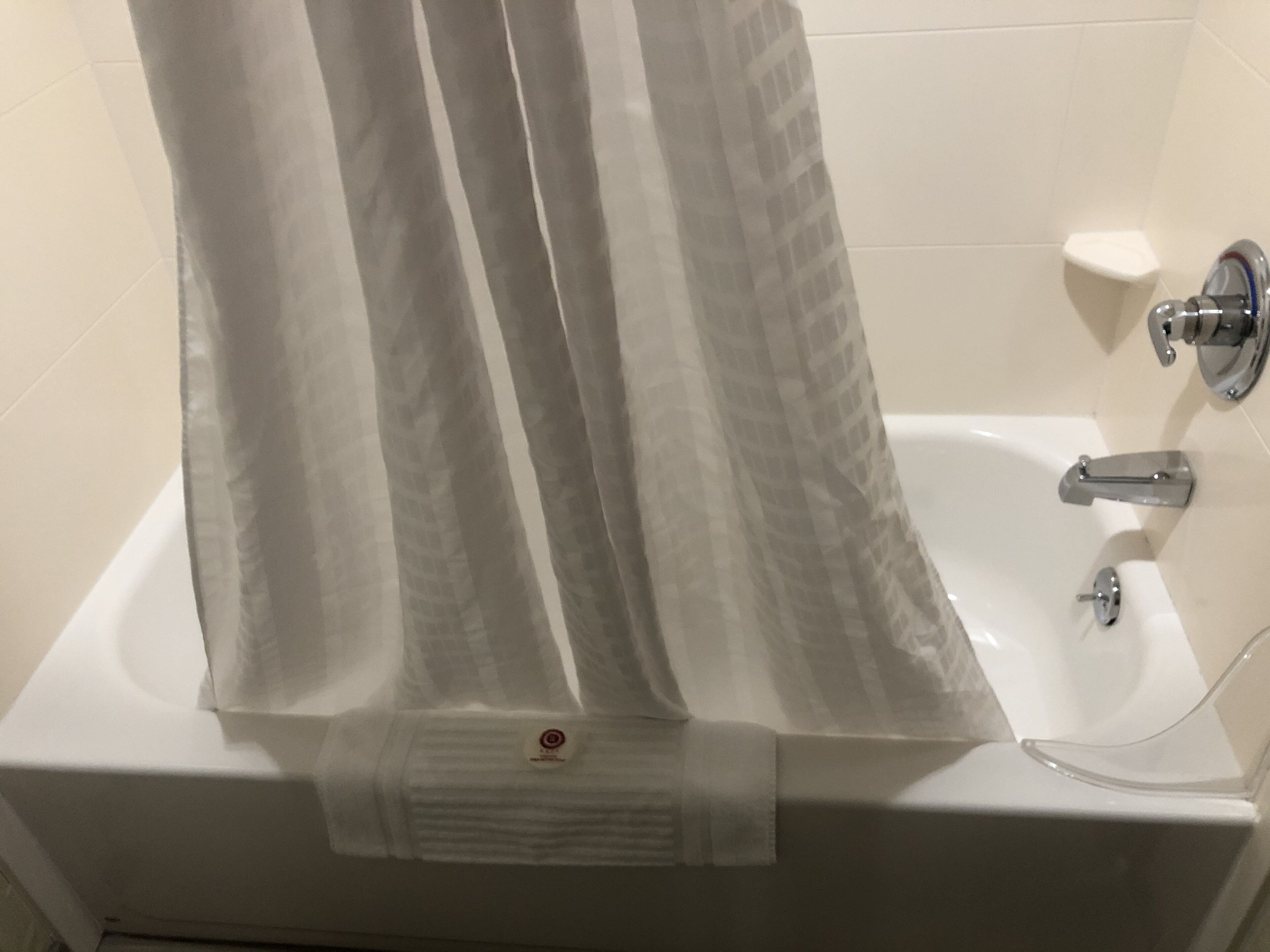 Uma banheira branca com cortina de chuveiro, chuveiro manual e porta-toalhas.