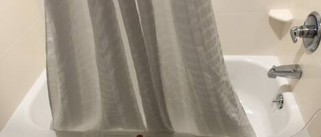 Une baignoire blanche avec un rideau de douche, une douchette et un porte-serviettes.