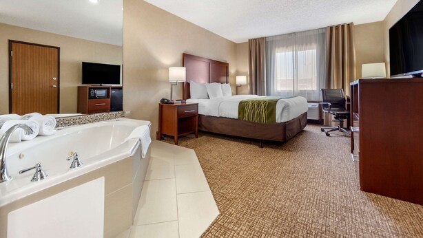 A hotel room with a large bed, a separate desk, a television, a bathroom with a bathtub, and a large mirror. - Comfort Inn Grand Island North (Grand Island)