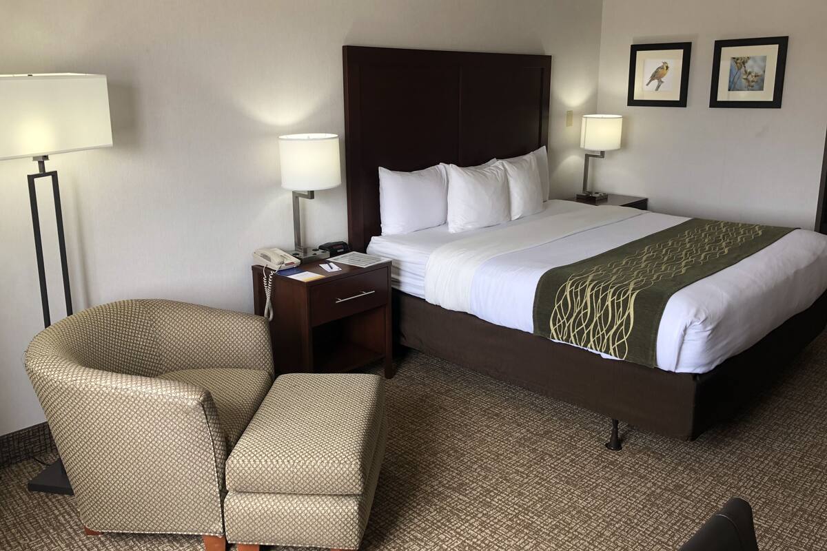 A hotel room with a large bed, two bedside tables, a chair, and two wall-mounted lamps.