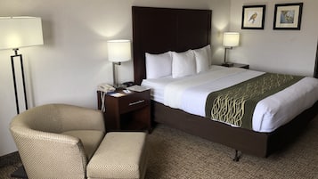 Une chambre d’hôtel avec un grand lit, deux tables de chevet, une chaise et deux lampes fixées au mur.