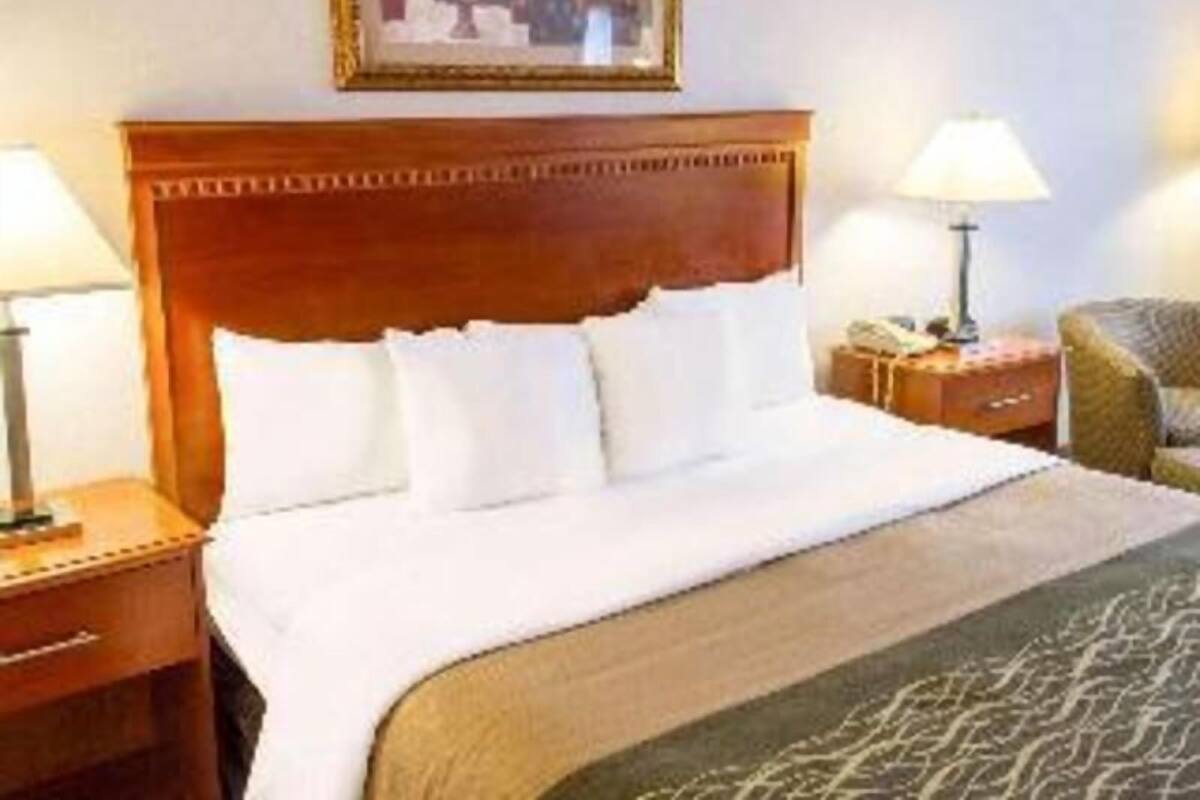 A hotel room with a wooden headboard, a bed with white linens, two bedside tables with lamps, and a framed picture on the wall.