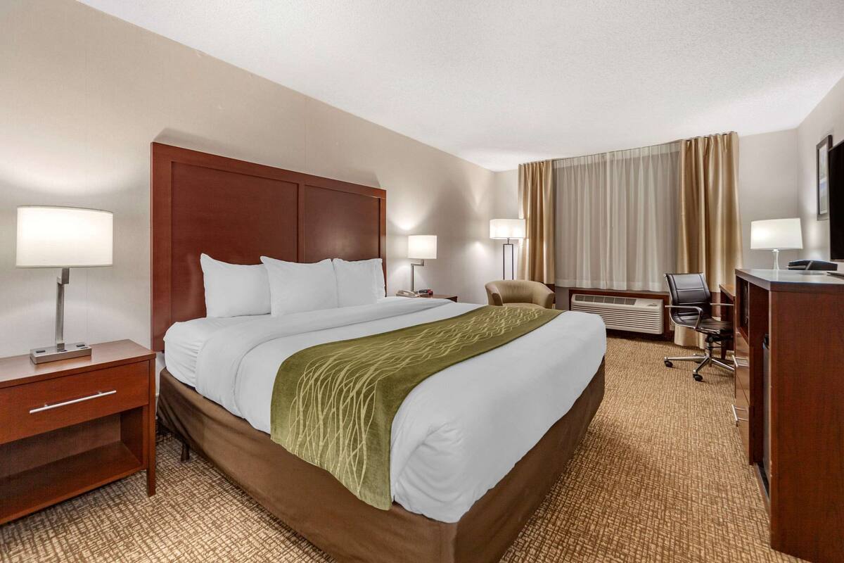 A hotel room with a large bed, bedside tables, a desk, a chair, and a television.