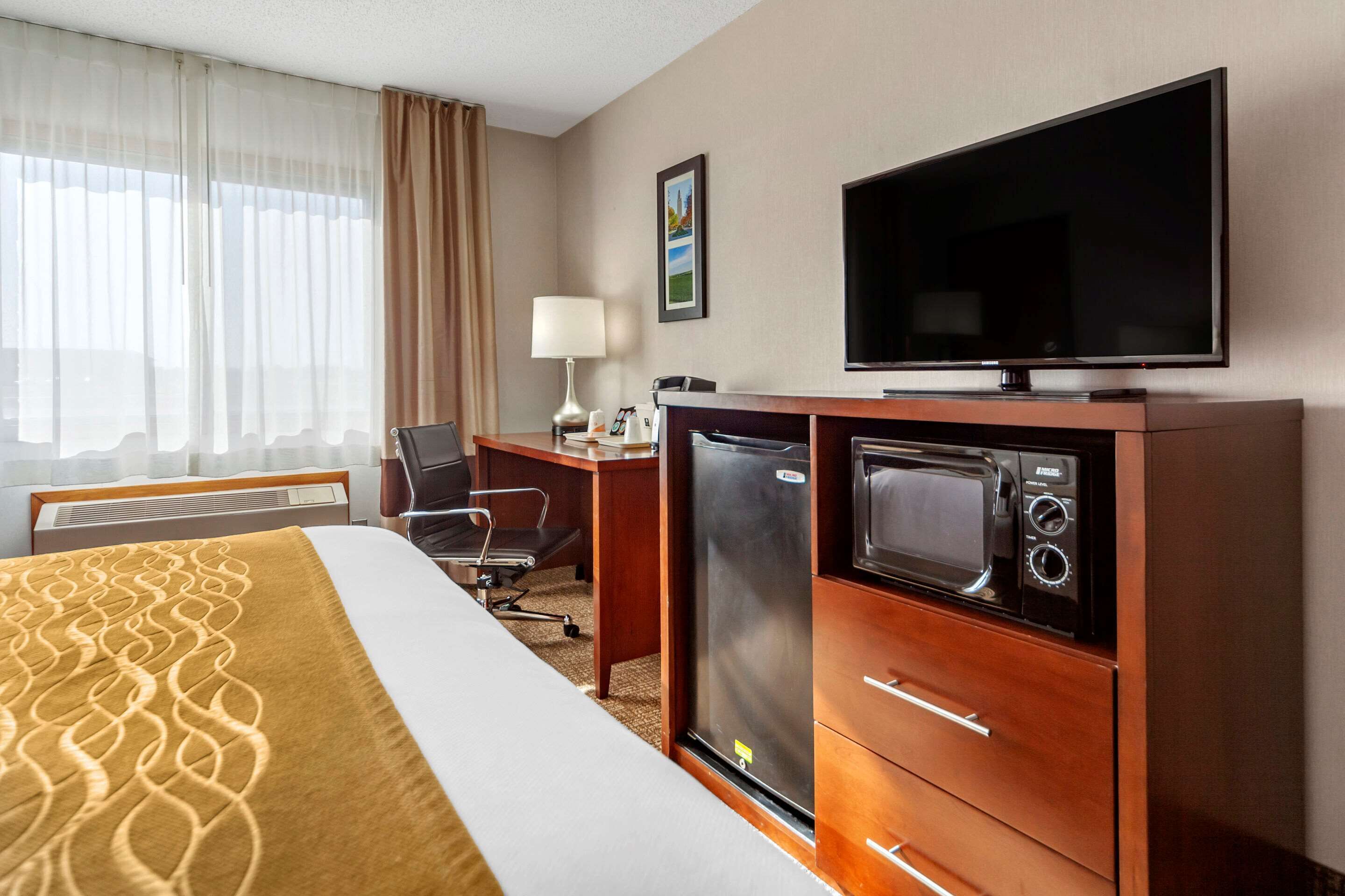 Una habitación de hotel con una cama, un escritorio con computadora, televisión, microondas y refrigerador.