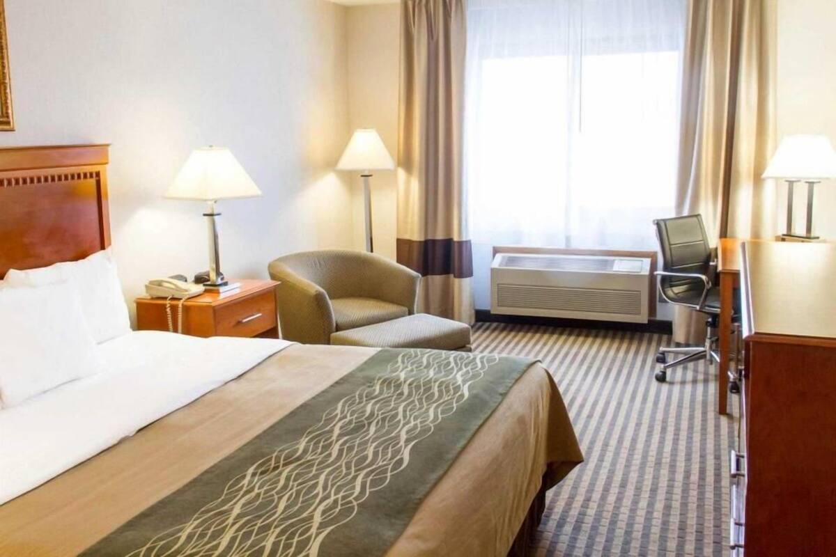 A hotel room with a bed, two chairs, a desk with a computer, a lamp, and a window with curtains.