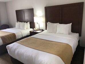 A hotel room with two beds, a nightstand, a lamp, and a telephone.