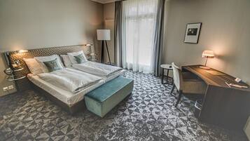 Habitación de hotel con una cama grande, un escritorio, una silla, una mesita, una lámpara y un cuadro en la pared.