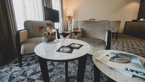 A hotel room with a sofa, two armchairs, a small table with wine glasses, a vase with flowers, and a magazine on a side table. - GLANDON Rooms Elite (Biel)