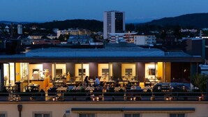 A rooftop restaurant with outdoor seating, a view of the cityscape, and a building in the background. - GLANDON Rooms Elite (Biel)