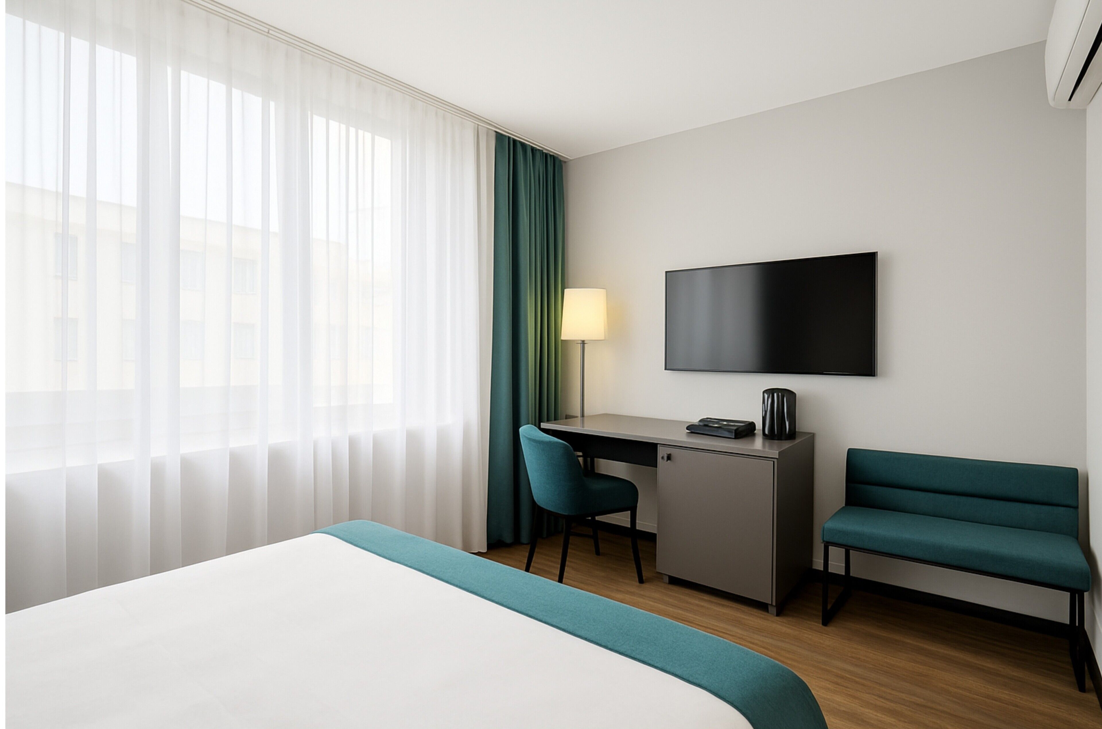 A hotel room with a bed, a desk with a chair, a TV, and a bench.